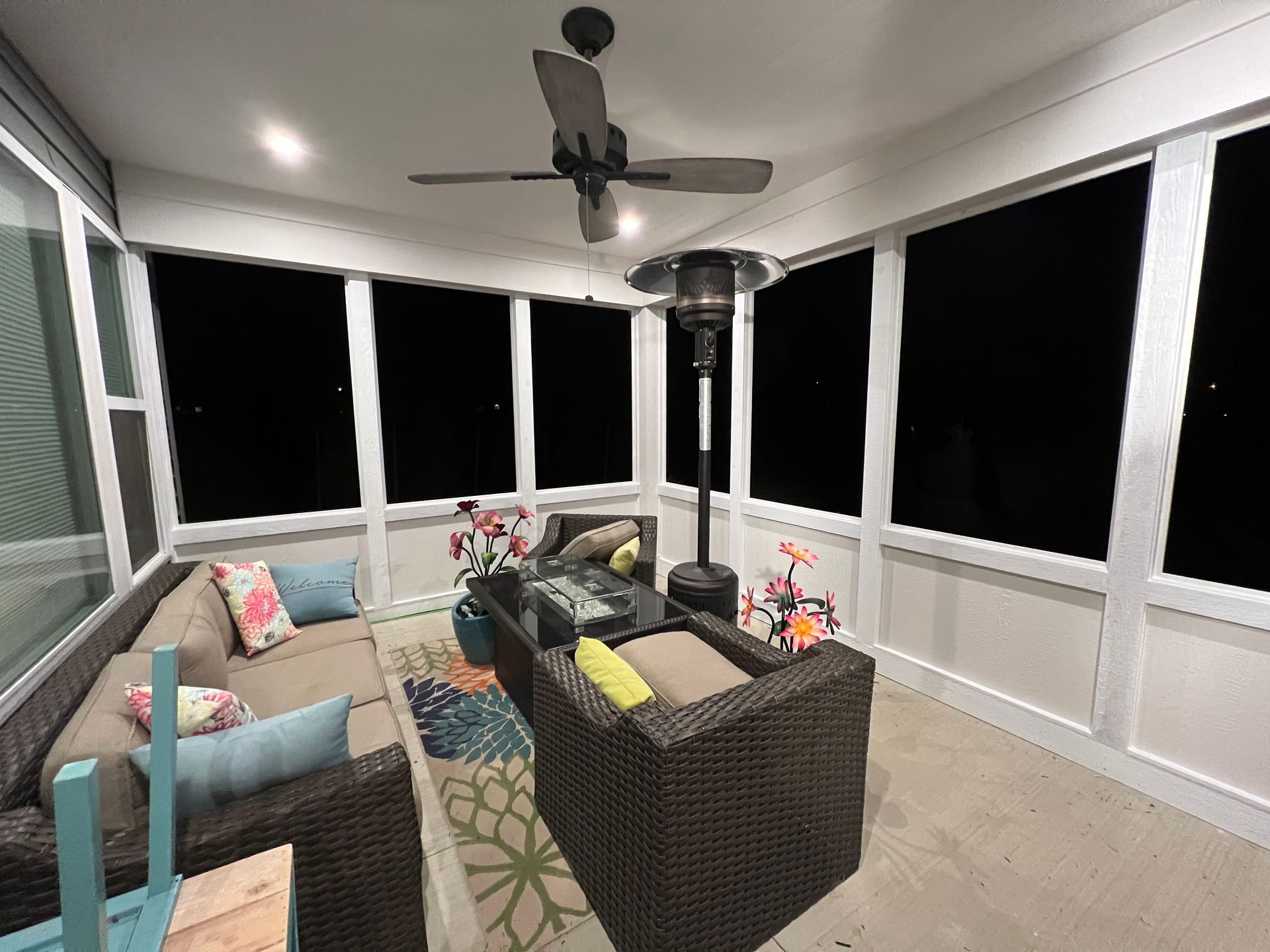 Screened porch with wicker seating, colorful cushions, and a ceiling fan at night