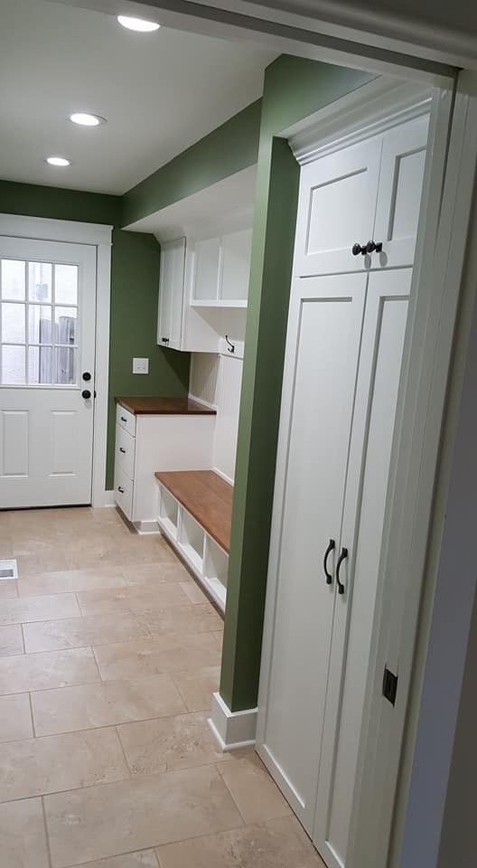 Hallway with green walls, white cabinets, built-in bench, and tiled floor leading to a door