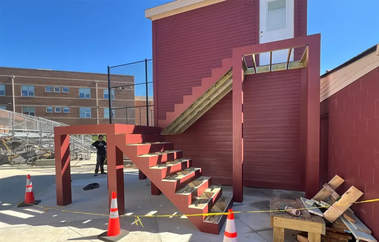 Outdoor red wooden staircase with landing and stairs beside a building, with orange traffic cones nearby