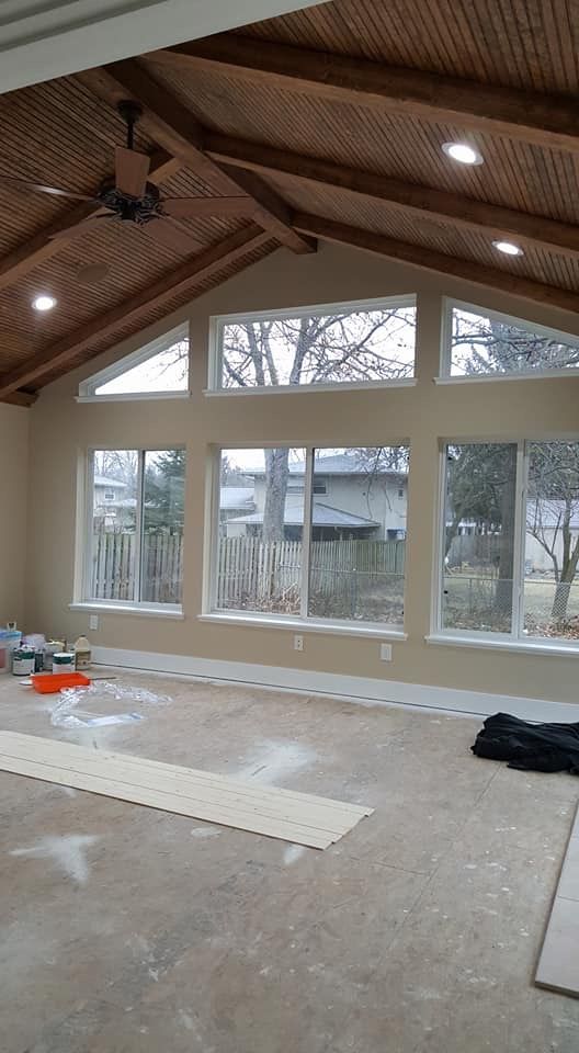 Spacious room under construction with vaulted wood ceiling, large windows, and tools on a bare floor.
