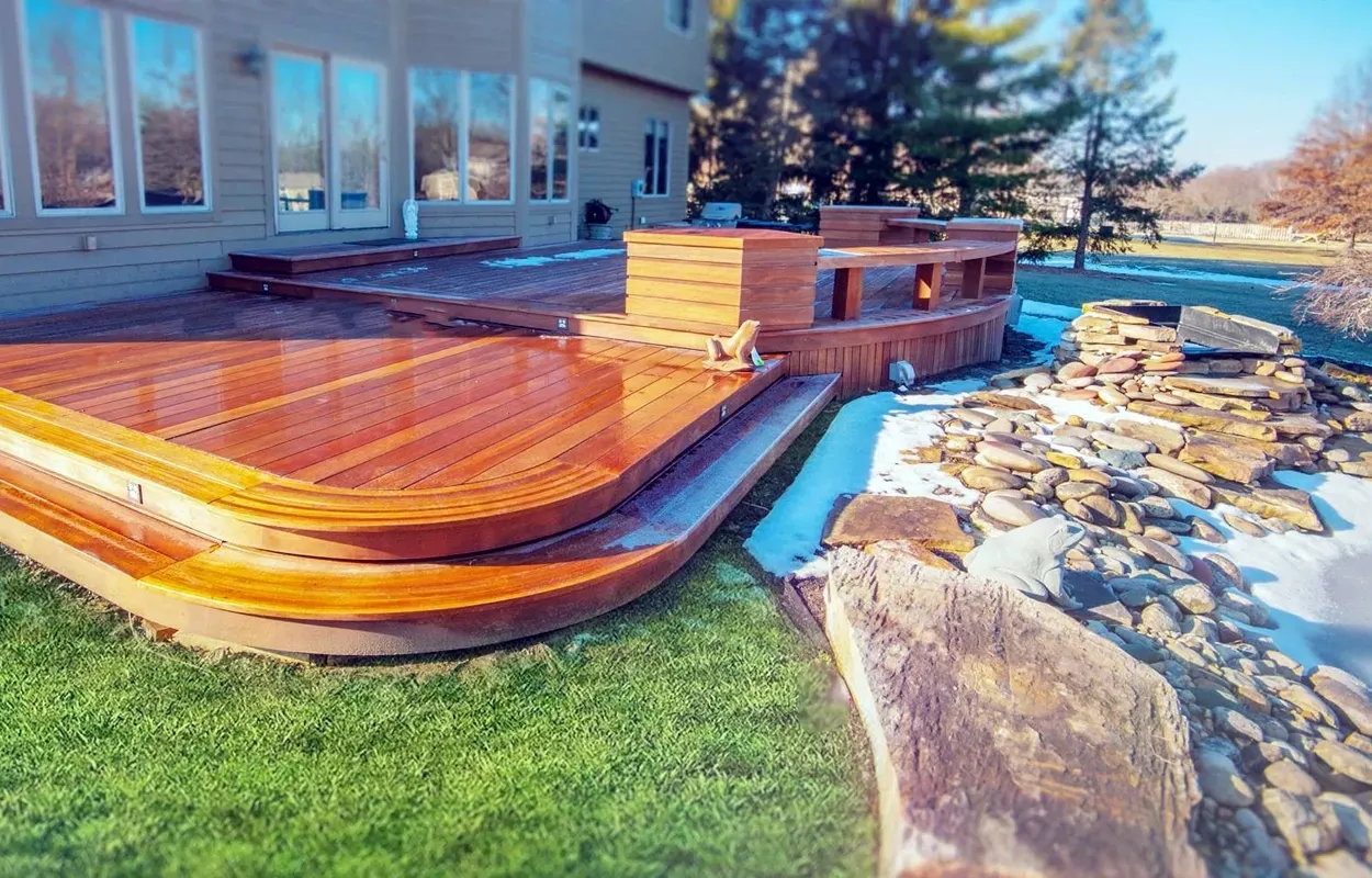 Wooden backyard deck with curved steps beside a house, overlooking grass and a stone garden path