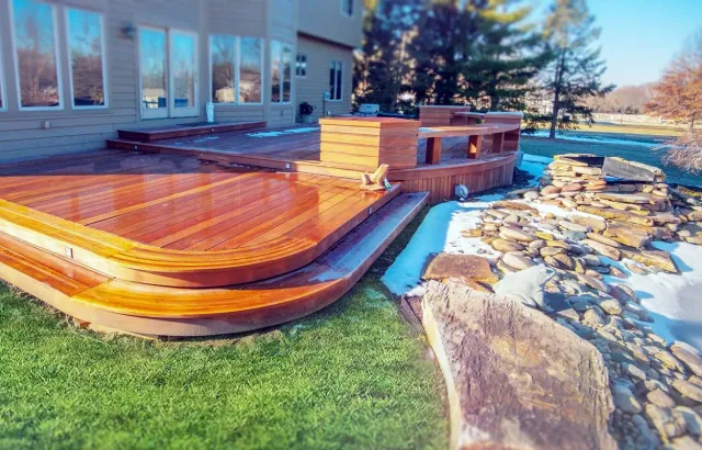 Wooden backyard deck with curved steps beside a house, overlooking grass and a stone garden path