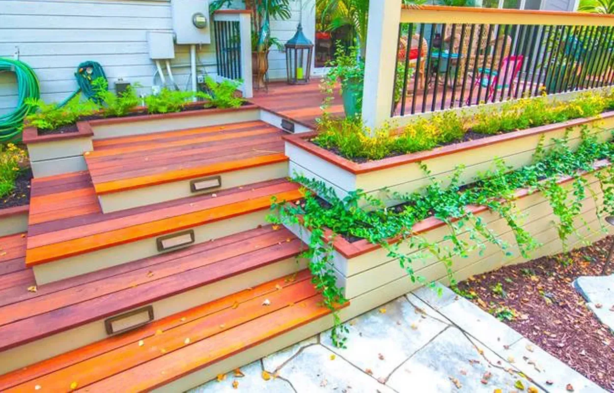 Front steps with orange wooden decking, stone walkway, and green vines beside a house