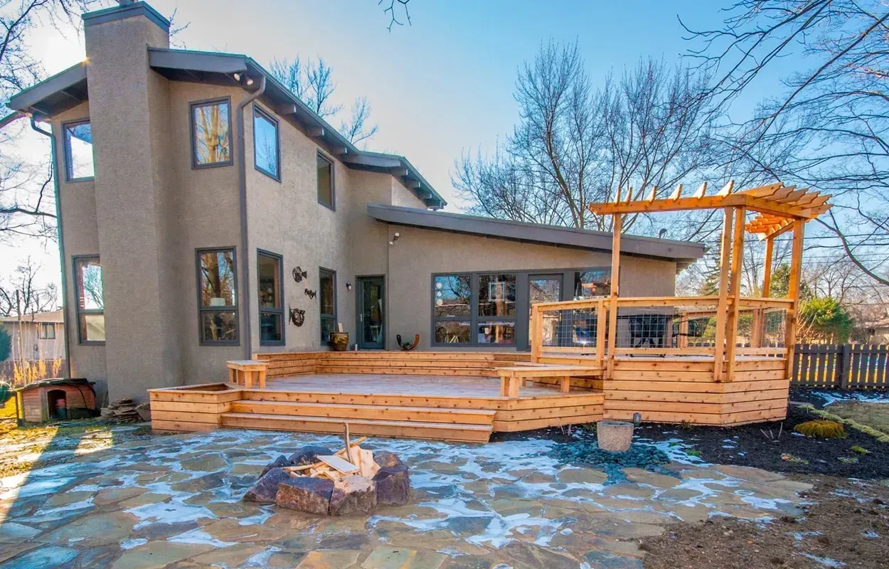 Modern house with a wooden deck and pergola in a snowy backyard