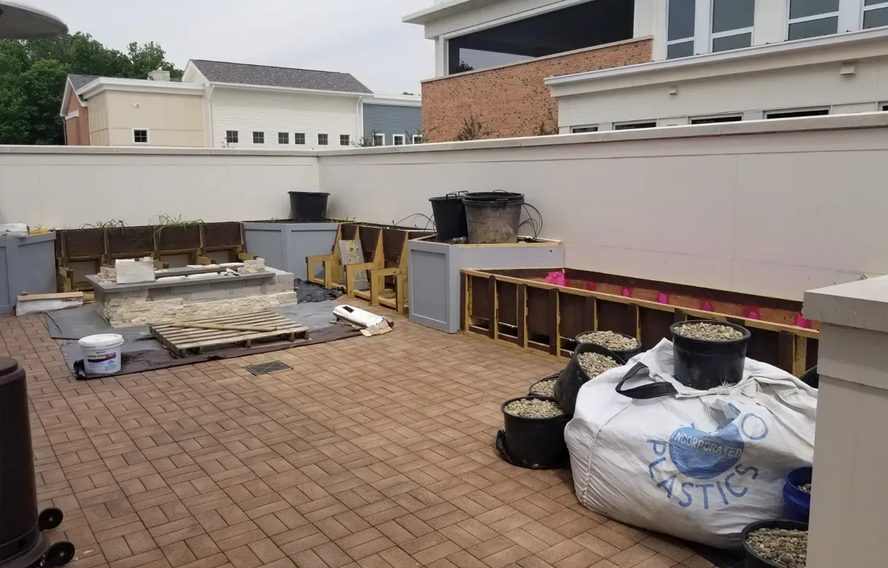 Patio with stacked construction materials, tools, and large bags beside a white wall.