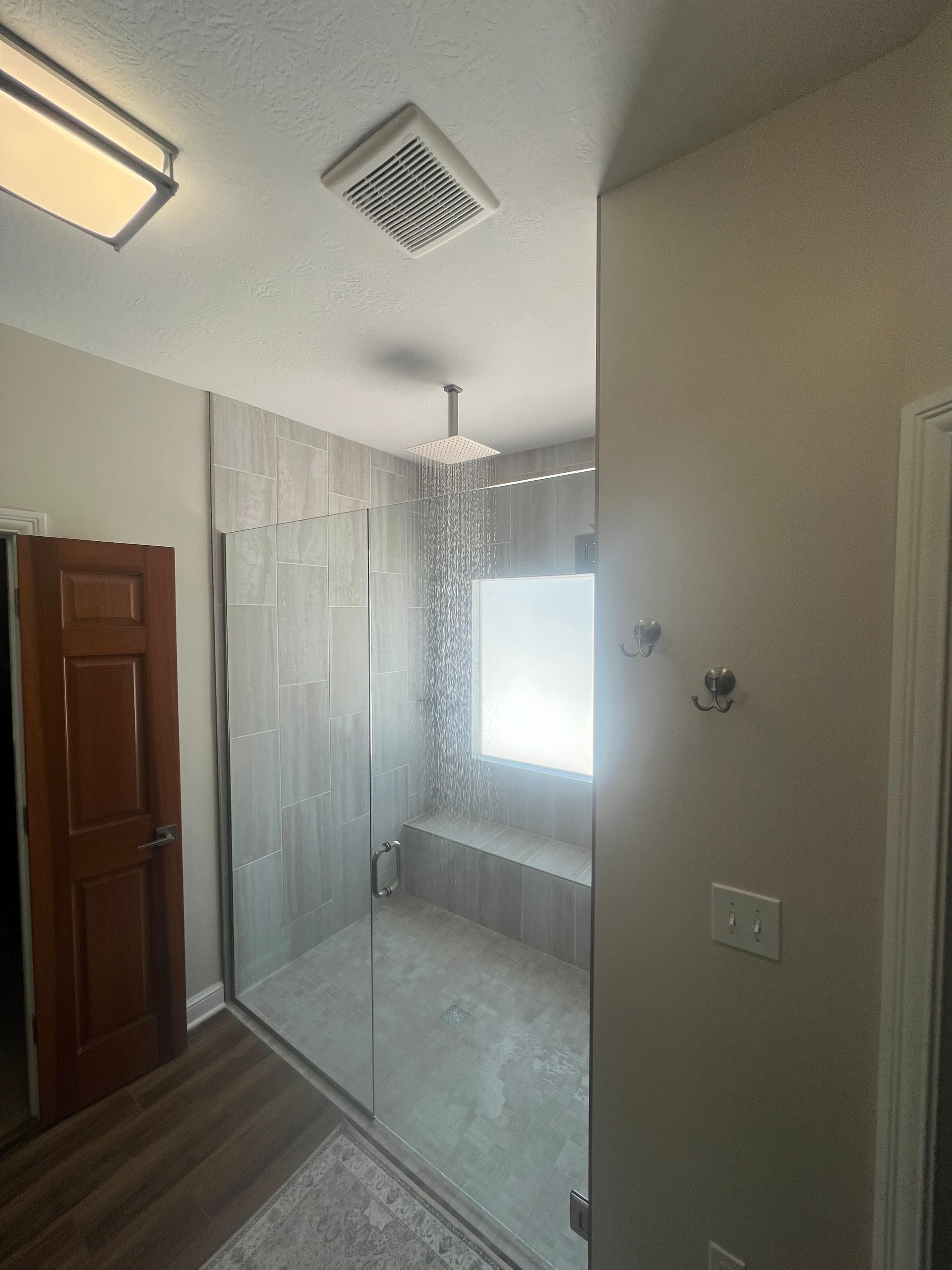 Bright bathroom with tiled shower, window seat, and wooden door, viewed from the entryway