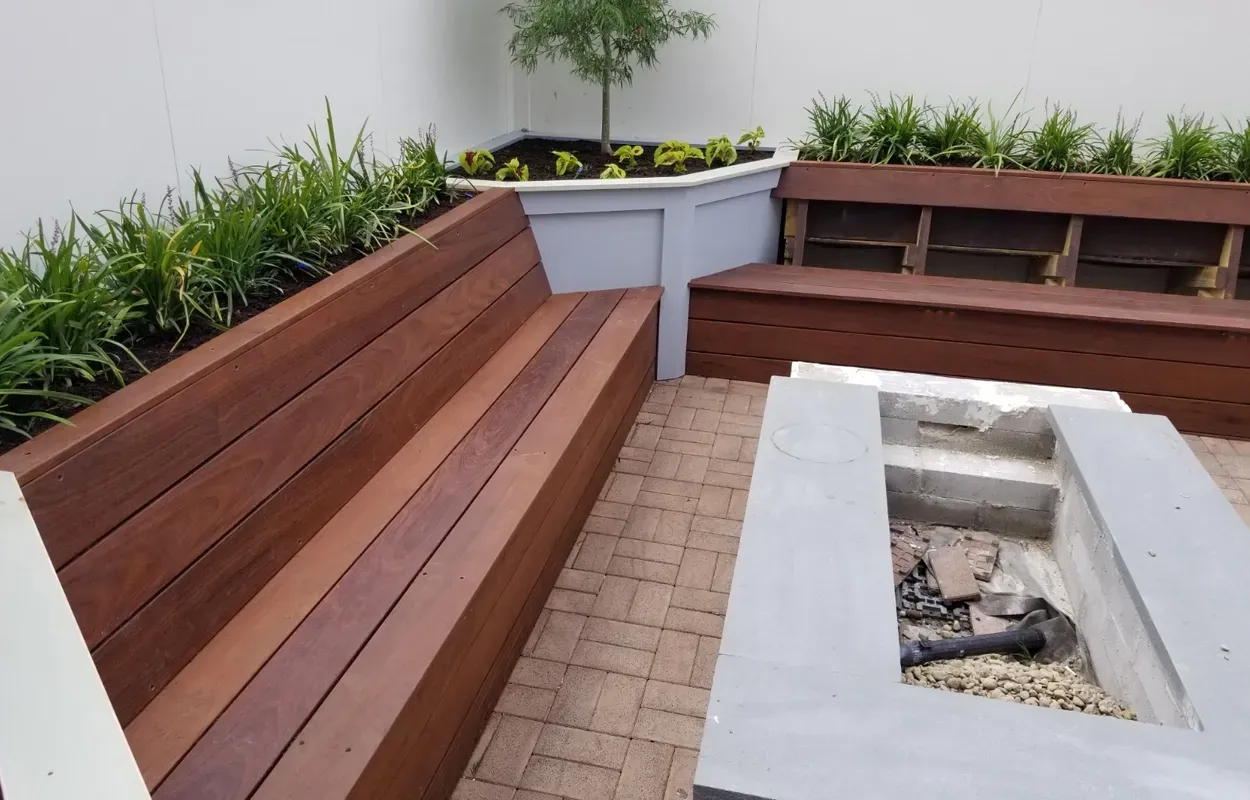 Outdoor patio with wooden benches, white planters, and a central concrete fire pit.