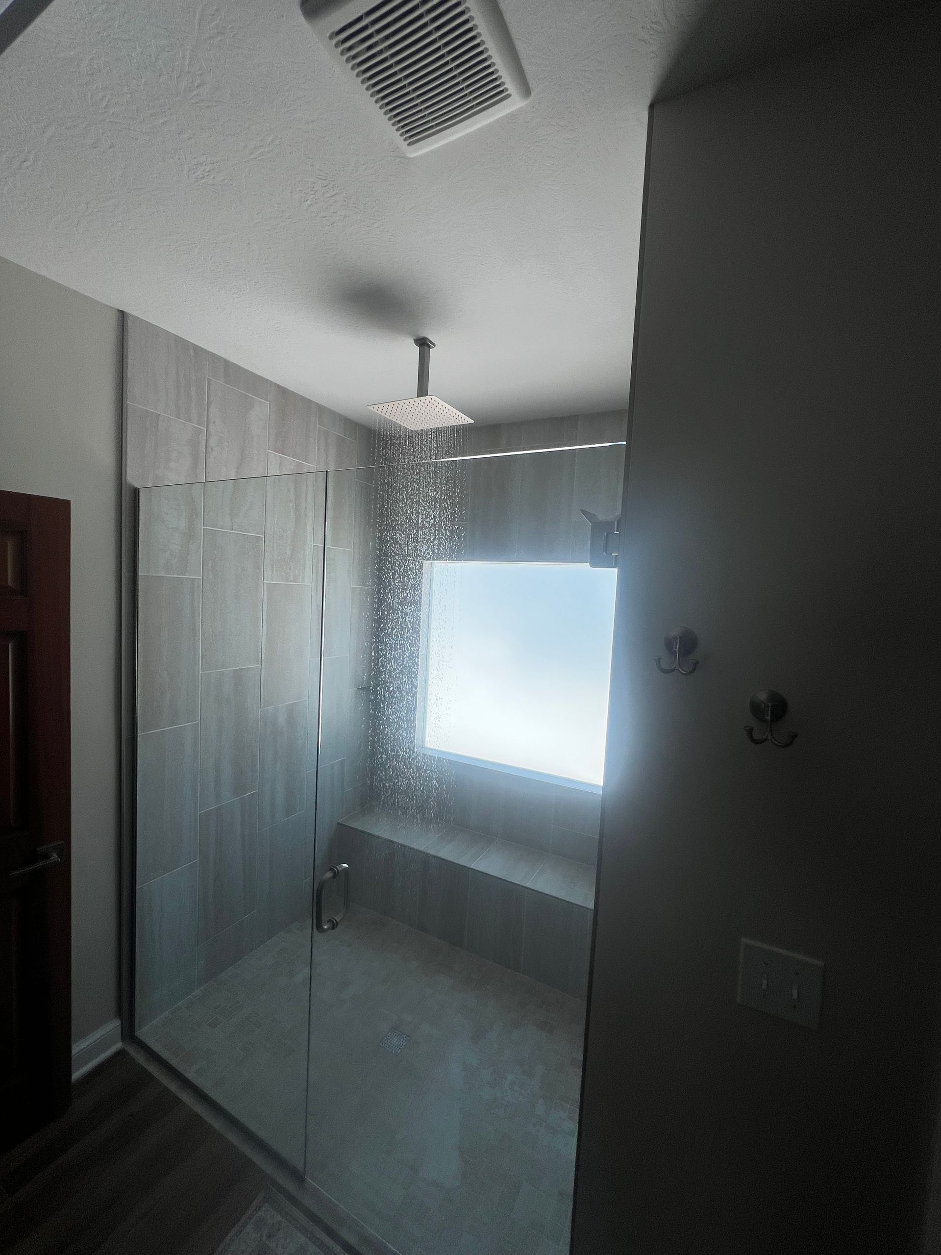 Dim bedroom with white closets, a bed by a bright window, and a ceiling fan.