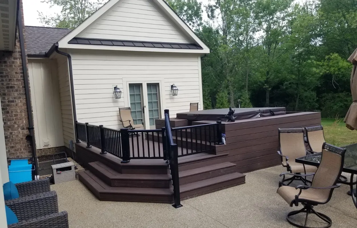 Back patio with dark railing, brick steps, and outdoor chairs beside a white house