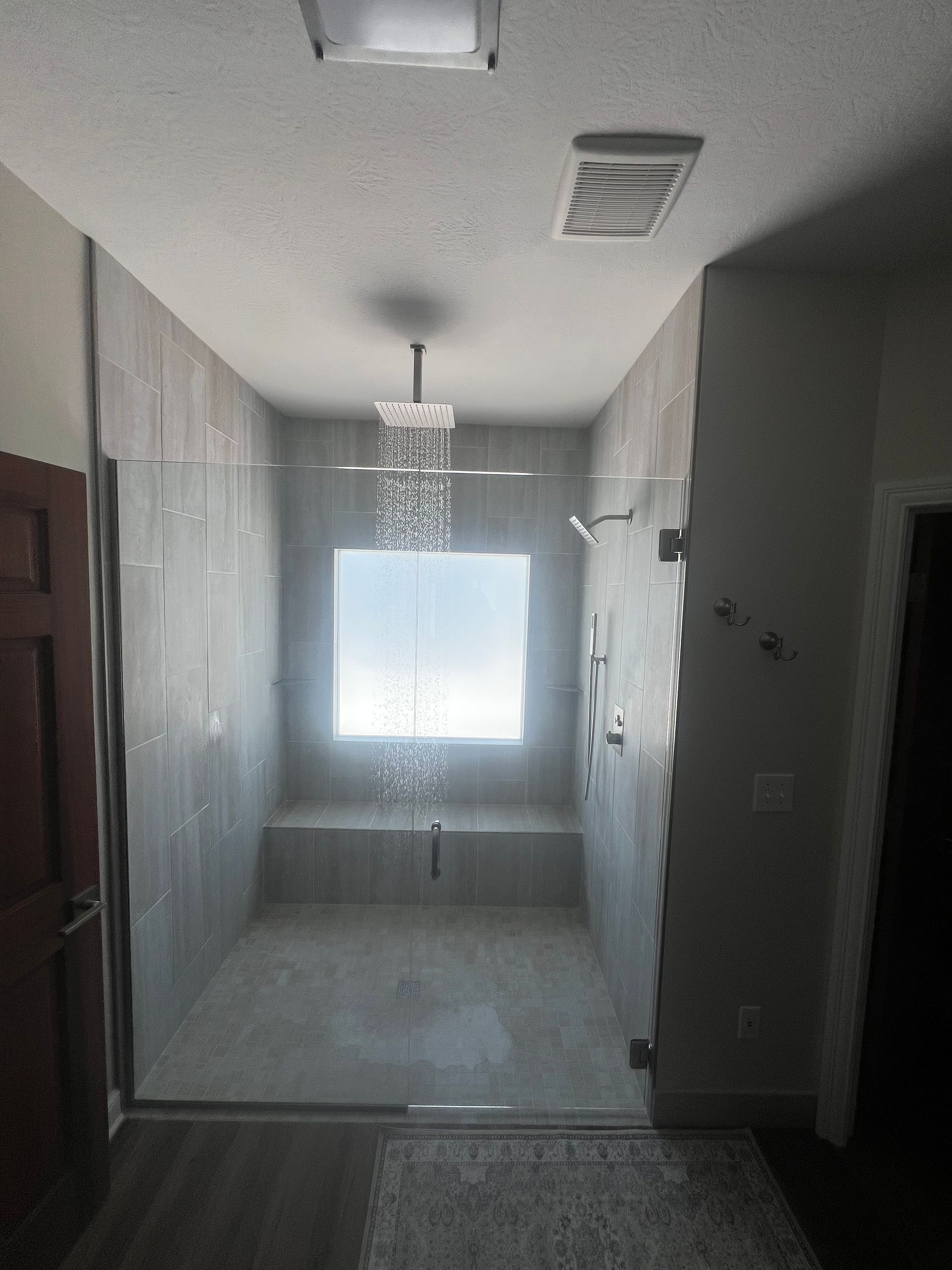 Narrow bathroom with gray tile, a hanging light fixture, and a bright window at the far end.