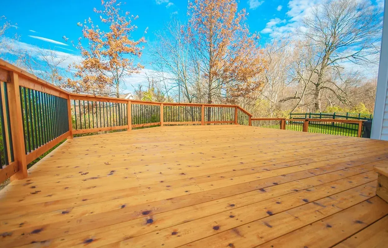 Wooden deck with railing and autumn trees under a bright blue sky