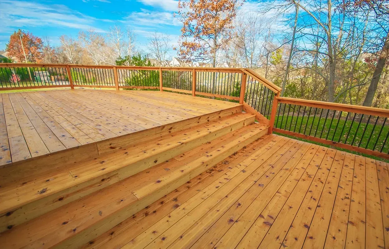 Wooden deck with steps and railing overlooking trees under a bright blue sky