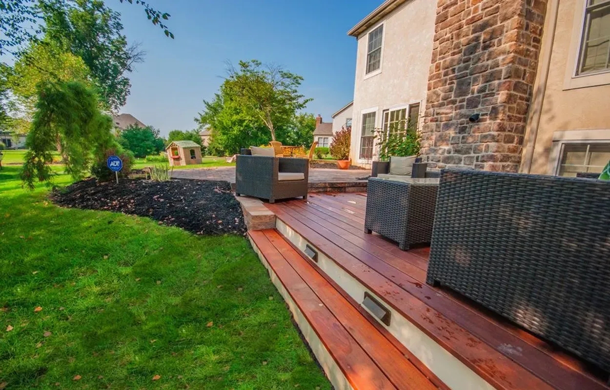 Backyard patio with wicker seating, wooden deck, lawn, and a house exterior