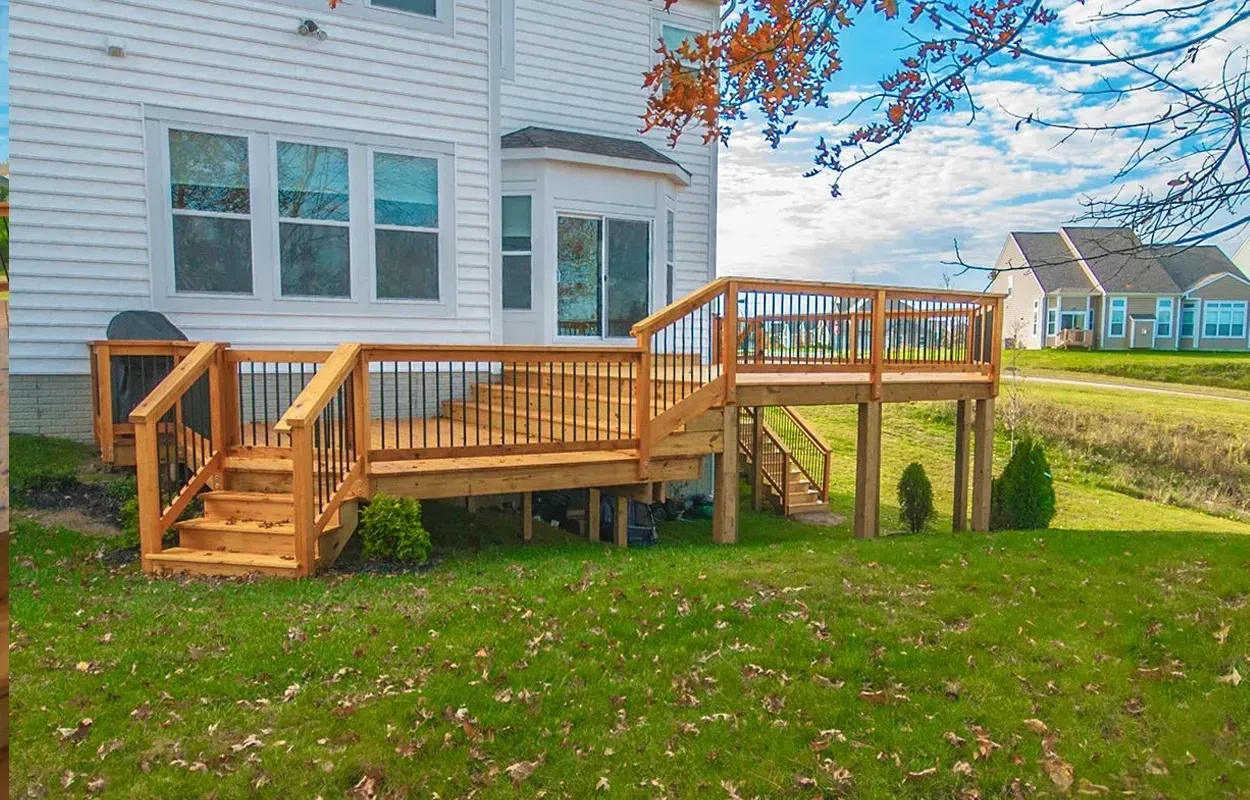 Wooden backyard deck with stairs attached to a white house under a blue sky.