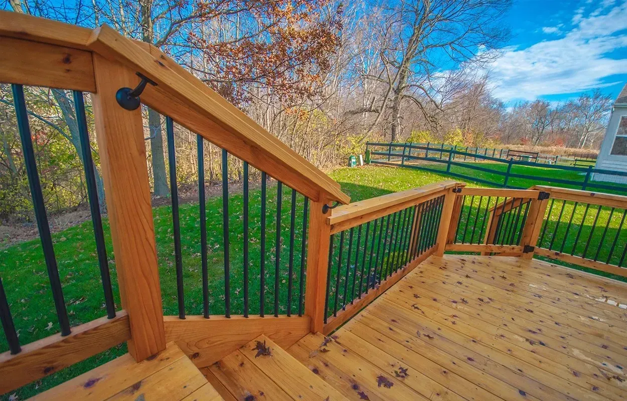 Wooden deck stairs and railing overlooking a green yard on a sunny day