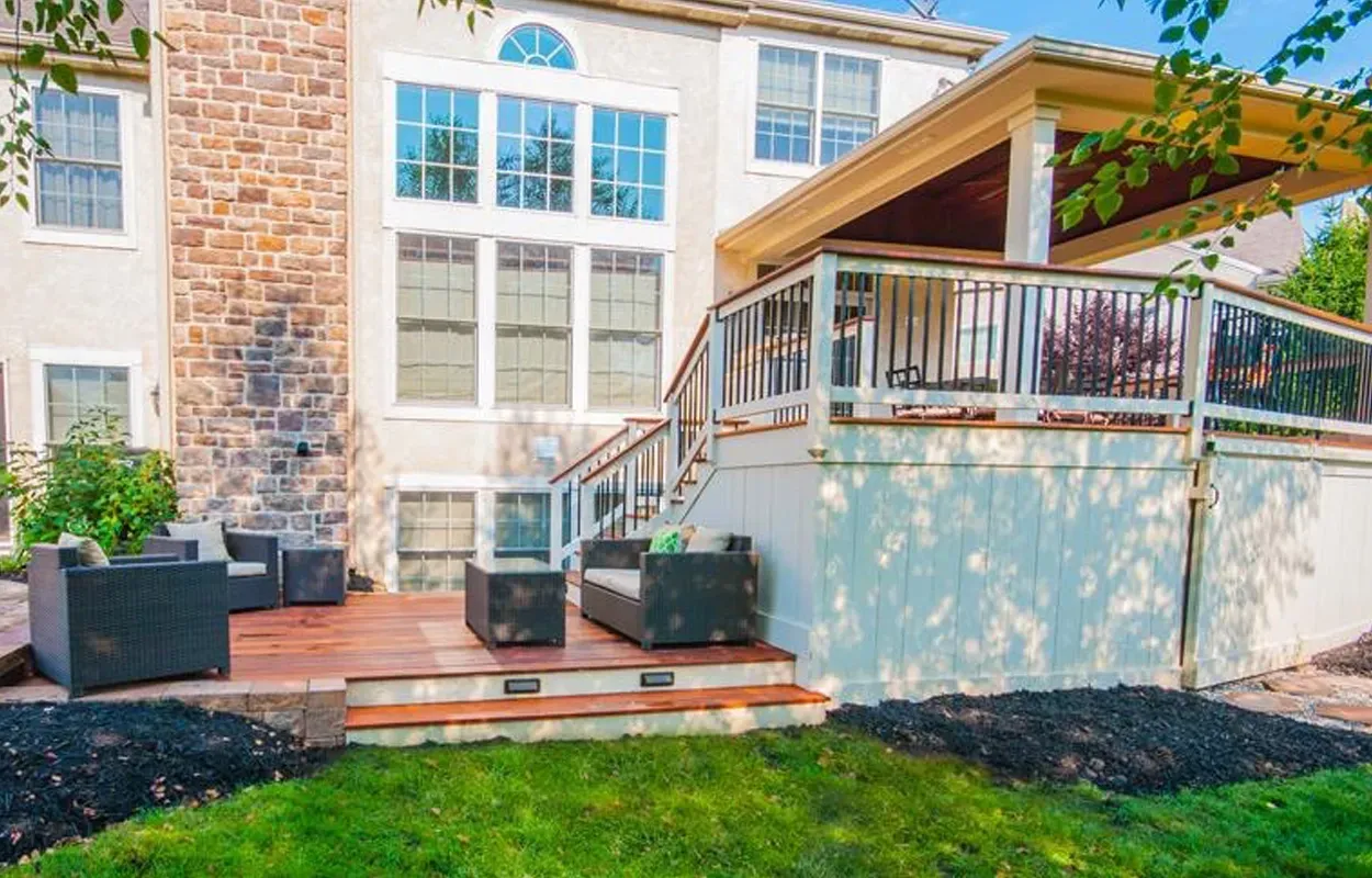 Backyard deck with wicker seating, stairs, pergola, and sliding glass doors on a house