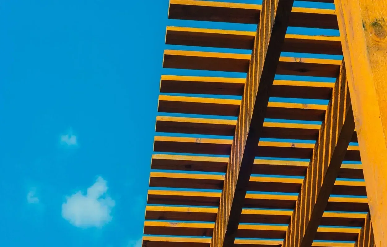 Blue sky with a small cloud beside a yellow building facade with repeating balconies and shadows