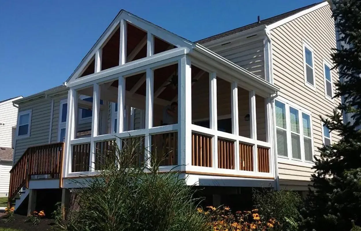 Modern beige house with a screened porch, white trim, and wooden railings in a sunny yard