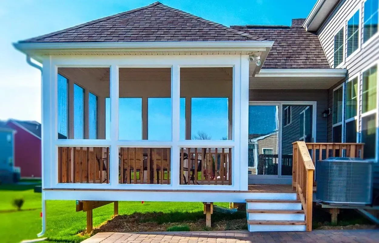 Raised screened porch with white trim, brown roof, and wooden steps on a sunny day
