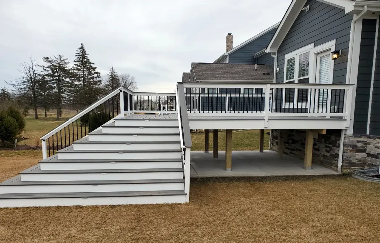 White wooden deck with stairs and railing attached to a gray house in a yard