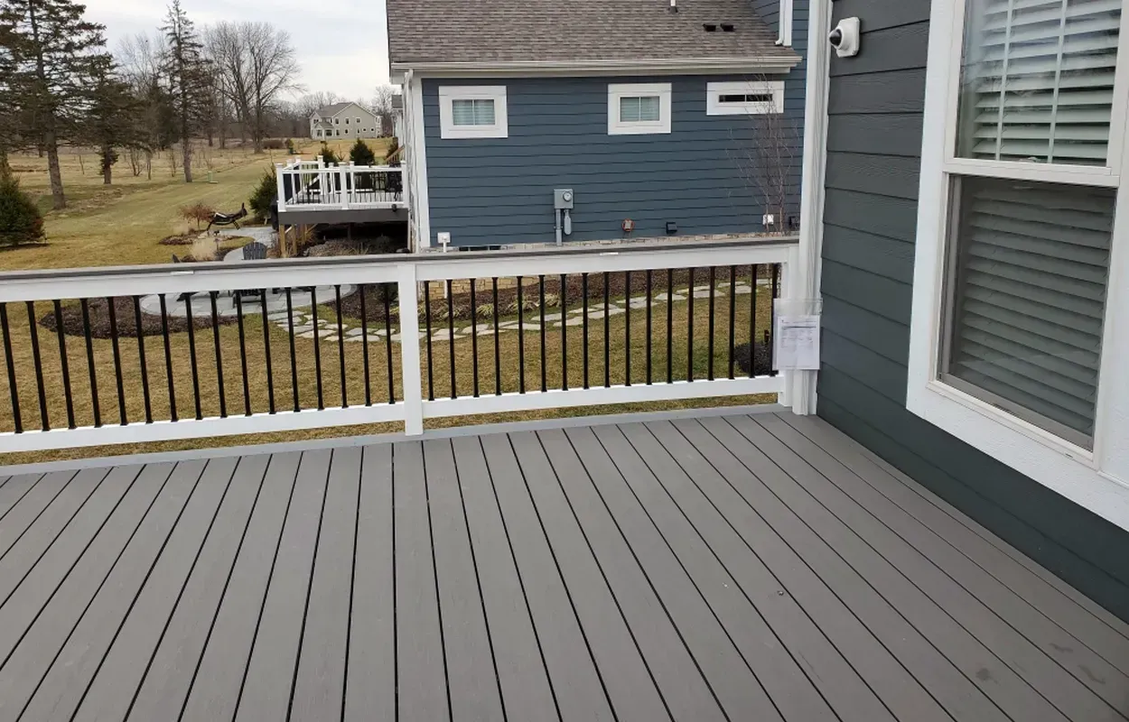 Gray deck with white railing overlooking a yard and blue house