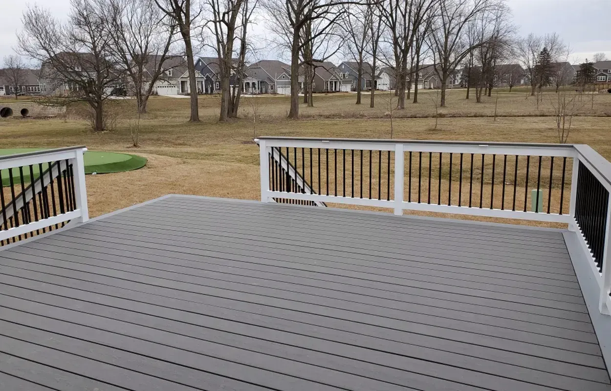 Wooden deck with white railings overlooking a grassy yard and leafless trees under an overcast sky