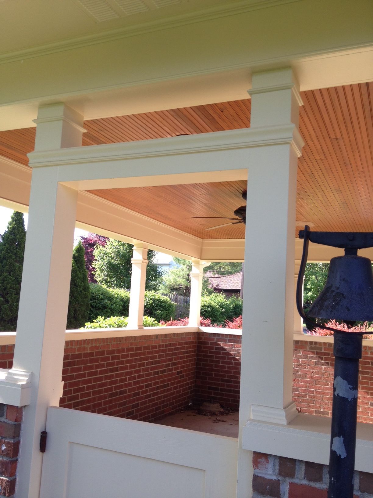 Covered porch with white columns, brick half-wall, and a blue bell hanging at the side.