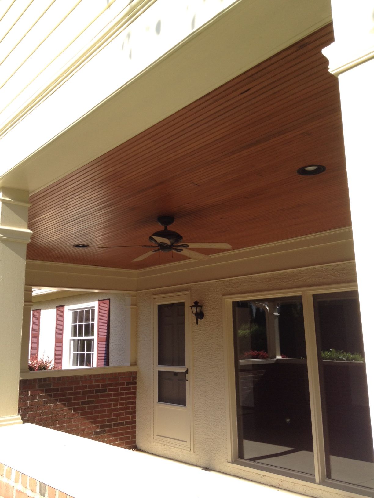 Covered porch with wood ceiling, ceiling fan, and glass doors beside a brick and cream house facade