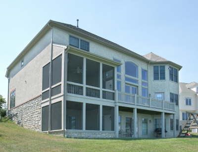 Two-story house with screened porches and blue-gray siding on a grassy hillside