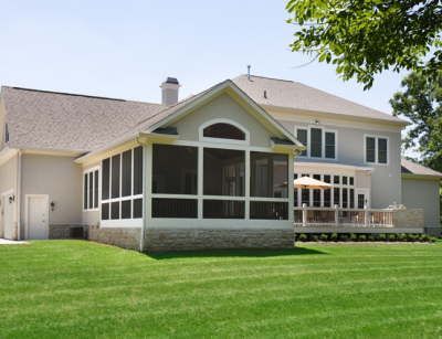 Suburban house with screened porch and screened deck on a green lawn under a clear sky