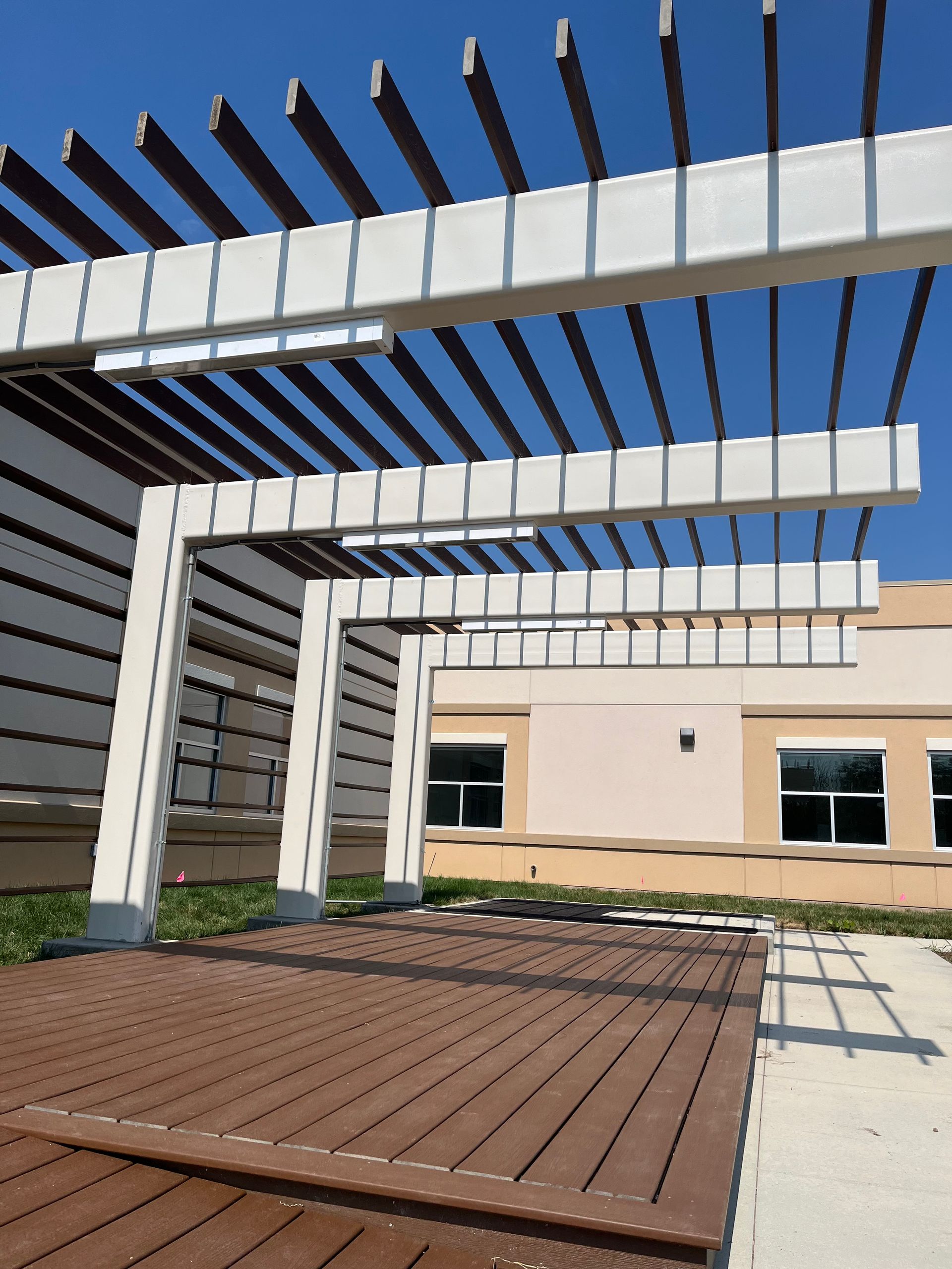 Modern patio with wooden pergola beams, raised deck seating, and a beige building in the background
