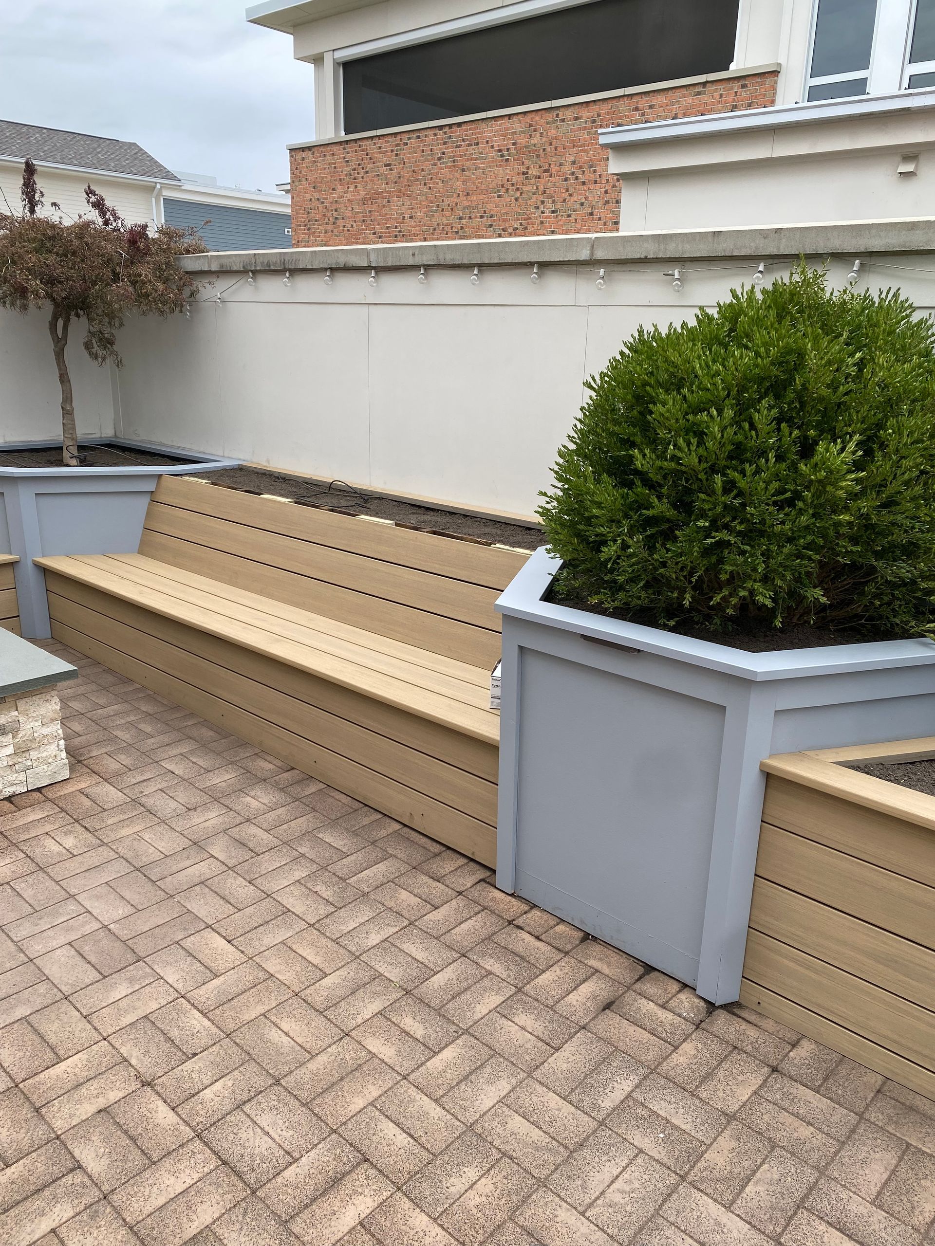 Courtyard patio with tan benches, gray planters, a green shrub, and white privacy wall under a house balcony