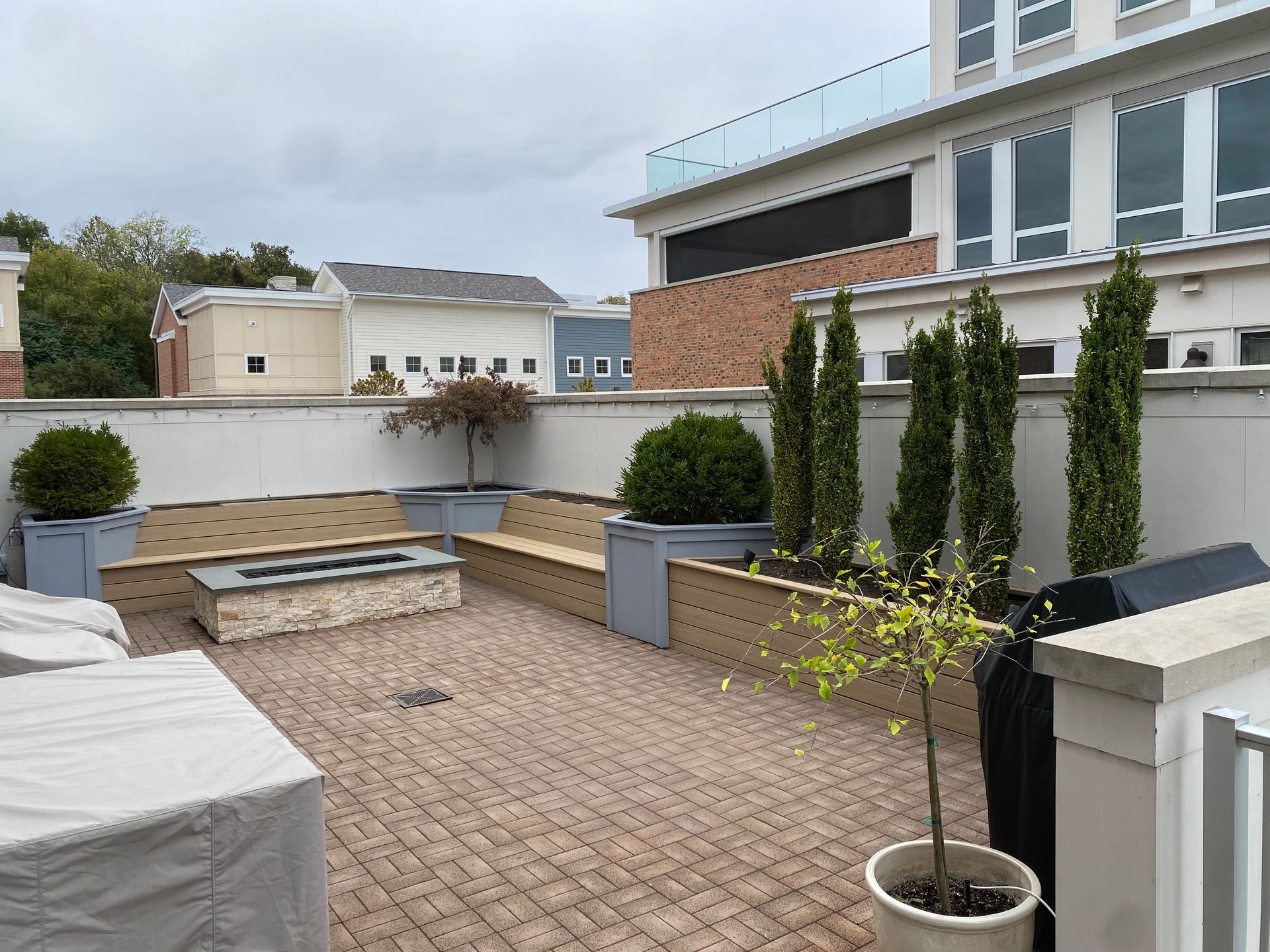 Modern paved courtyard with raised planters, potted shrubs, and a townhouse facade