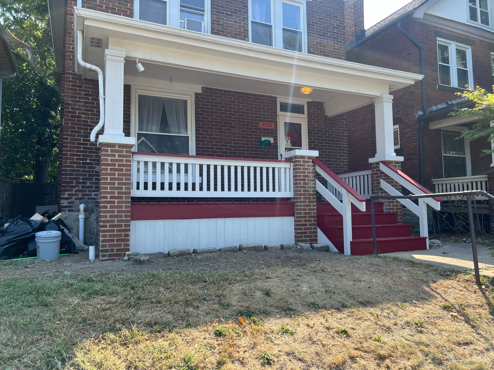 Brick house with a red-and-white front porch, stairs, and small yard in daylight