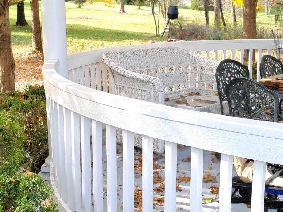 White porch railing with wicker chairs on a sunlit deck in a wooded yard