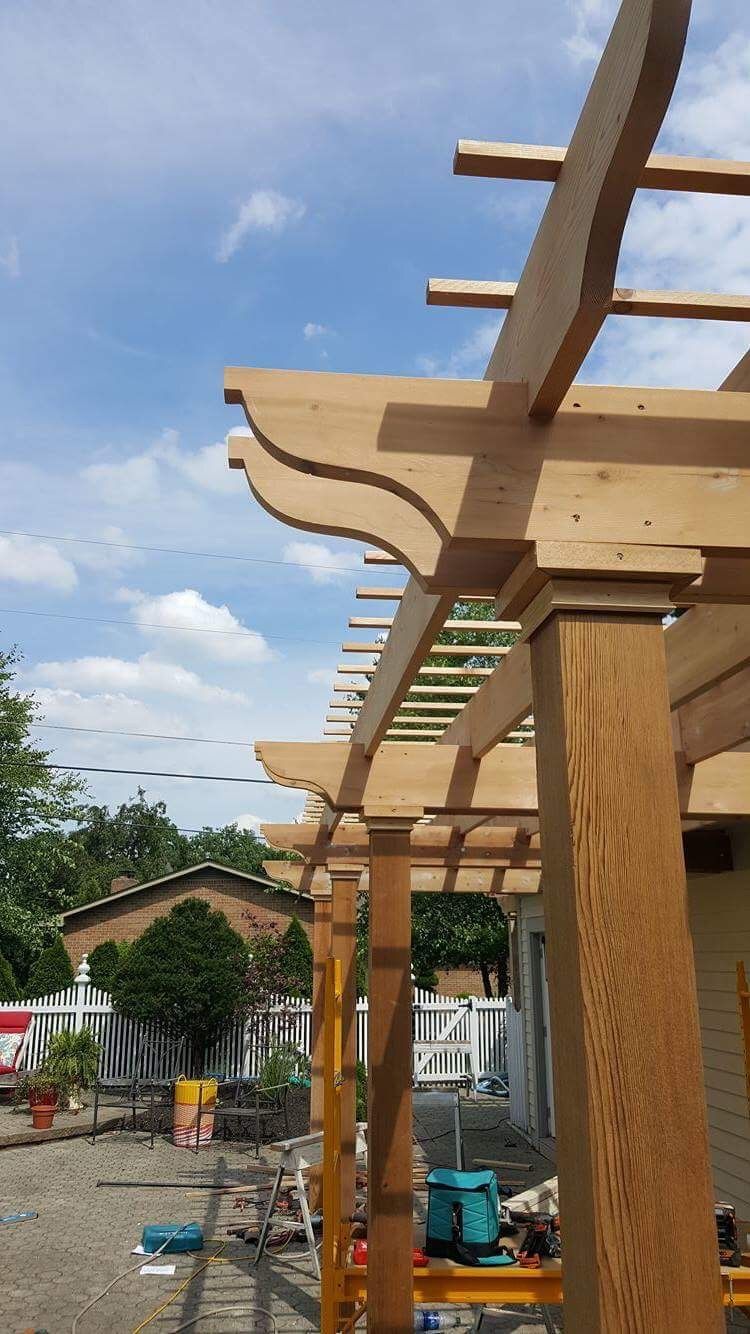 Wooden pergola being built beside a house under a blue sky.