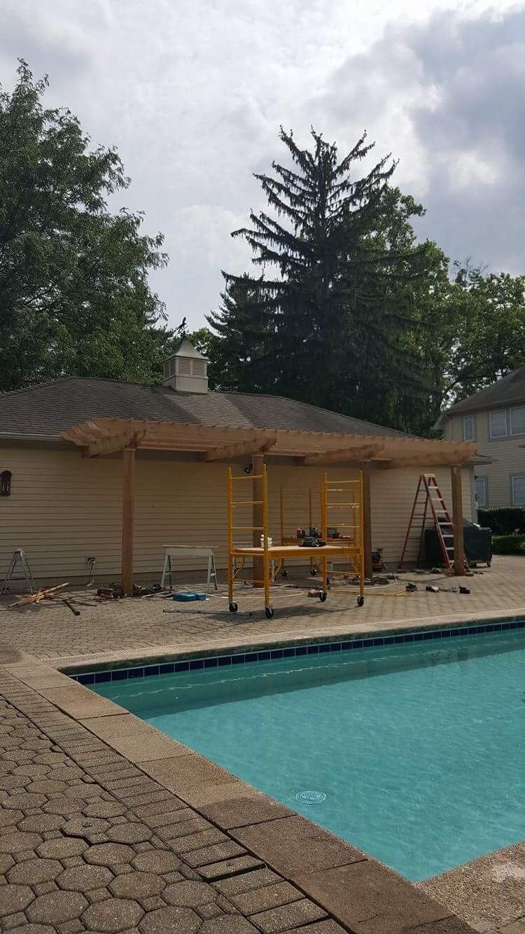Backyard pool beside a wooden deck and small shed, with a ladder and cloudy sky overhead