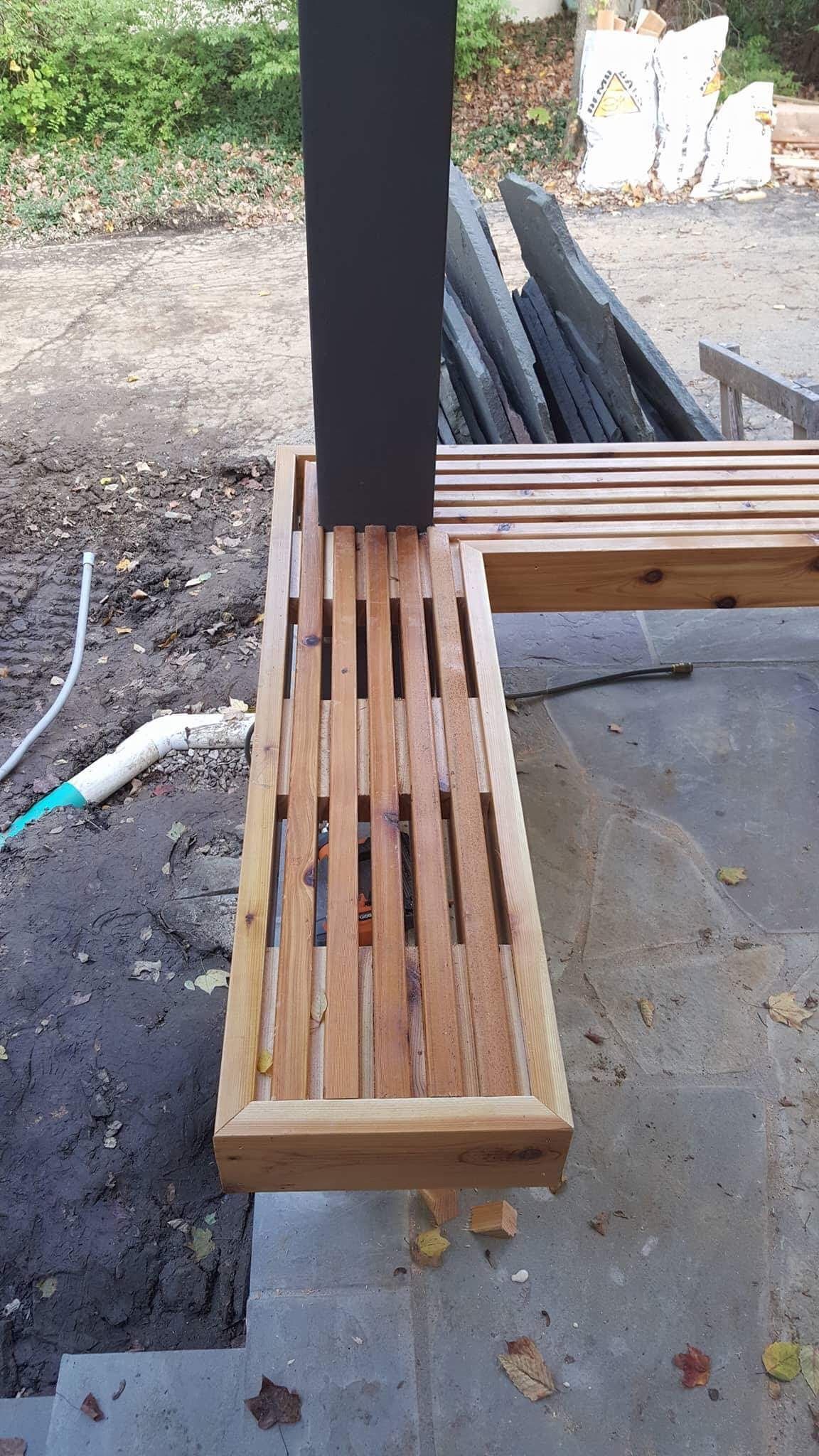 Wooden slatted bench wrapping around a black post on a concrete patio.