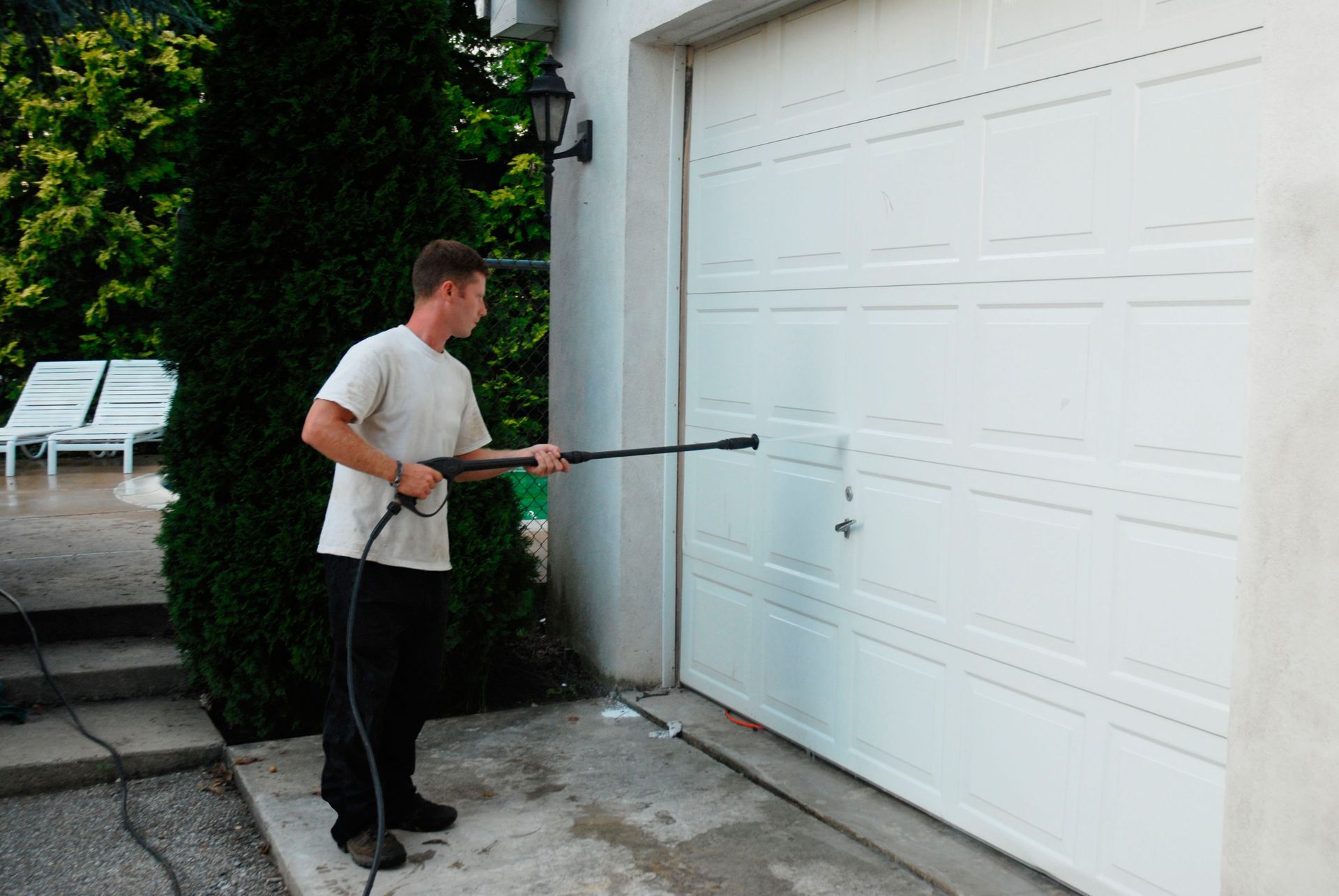 Man power washing a white garage door outside a house.