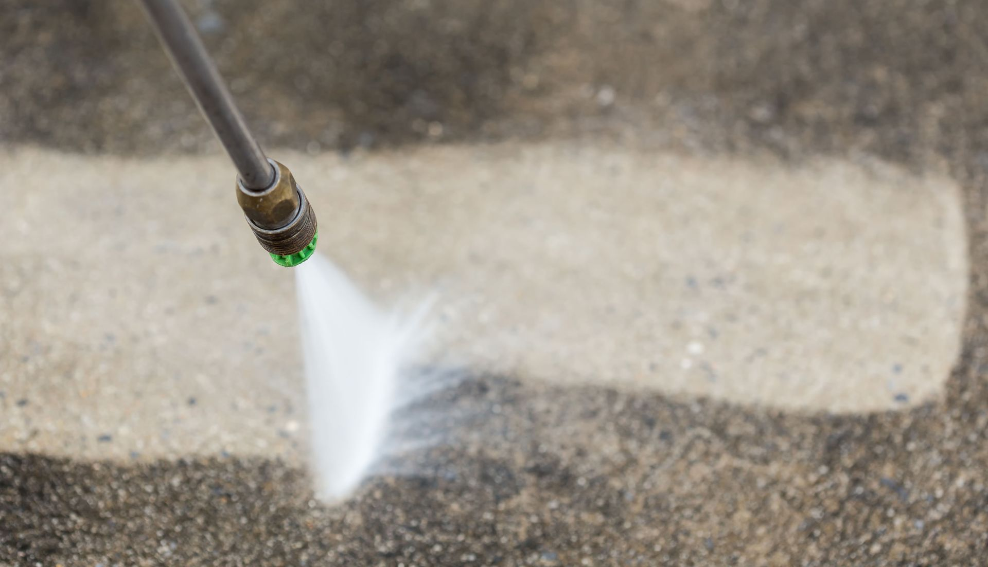 Pressure washer cleaning a concrete surface; a stream of water sprays a white line.