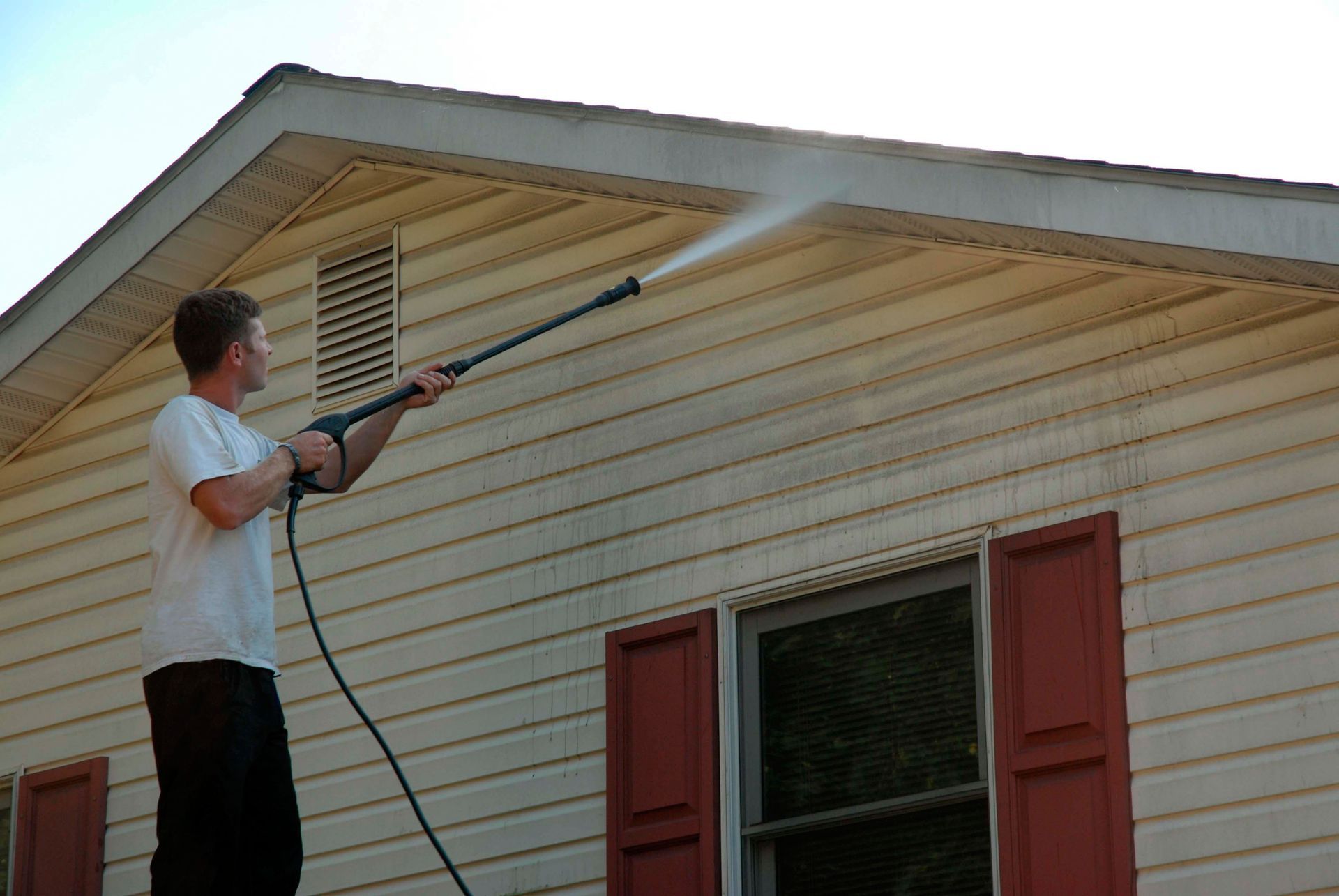 Man pressure washing a white garage door outside a house.