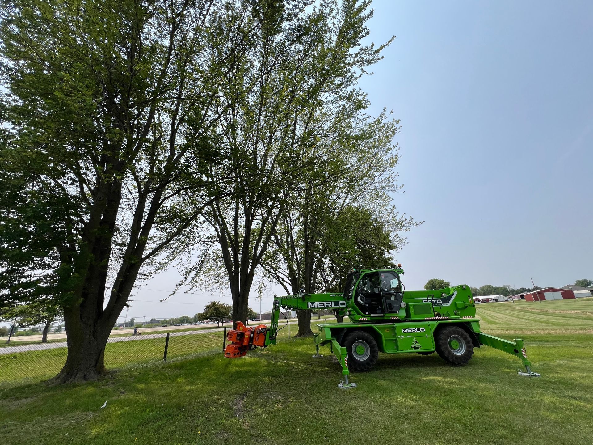 A green tractor is parked in a grassy field next to trees.