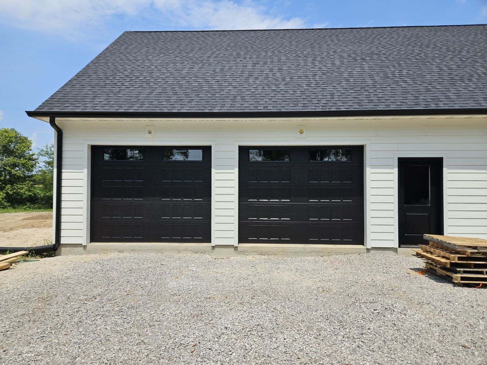 A garage with three black garage doors and a black roof.