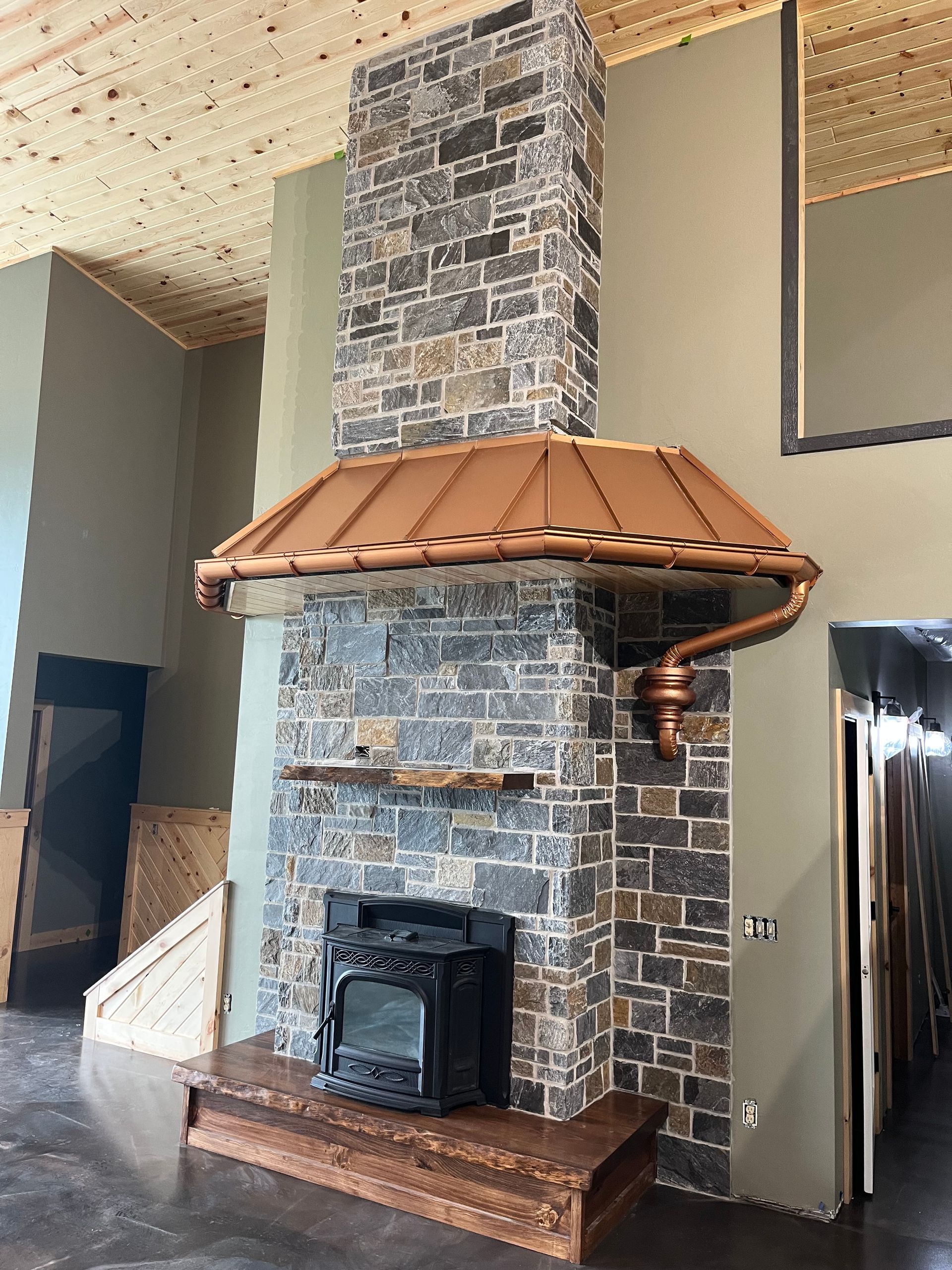 Stone fireplace with copper hood, black firebox, and wooden hearth.