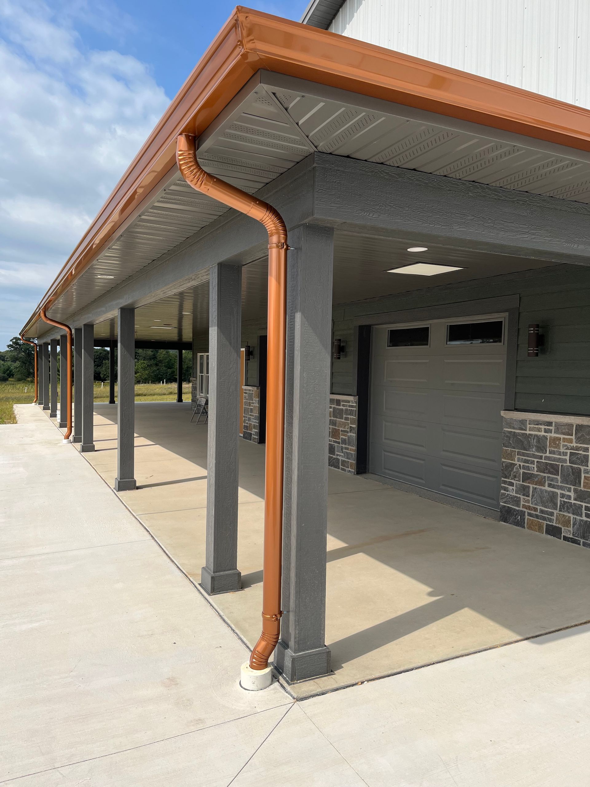 Exterior view of a building with a covered walkway and brown gutters, gray pillars, and a garage door.