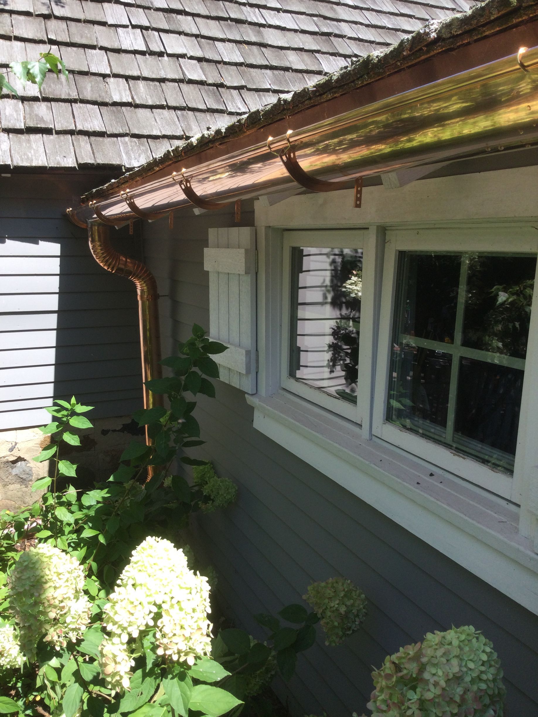There is a copper gutter on the side of a house next to a window.