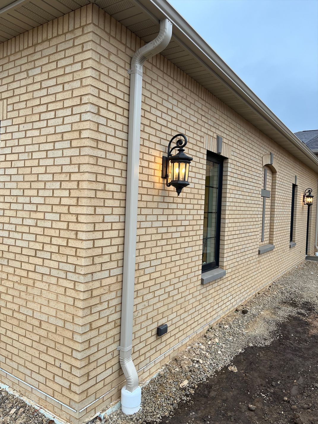 A brick house with a gutter and a lamp on the side of it.