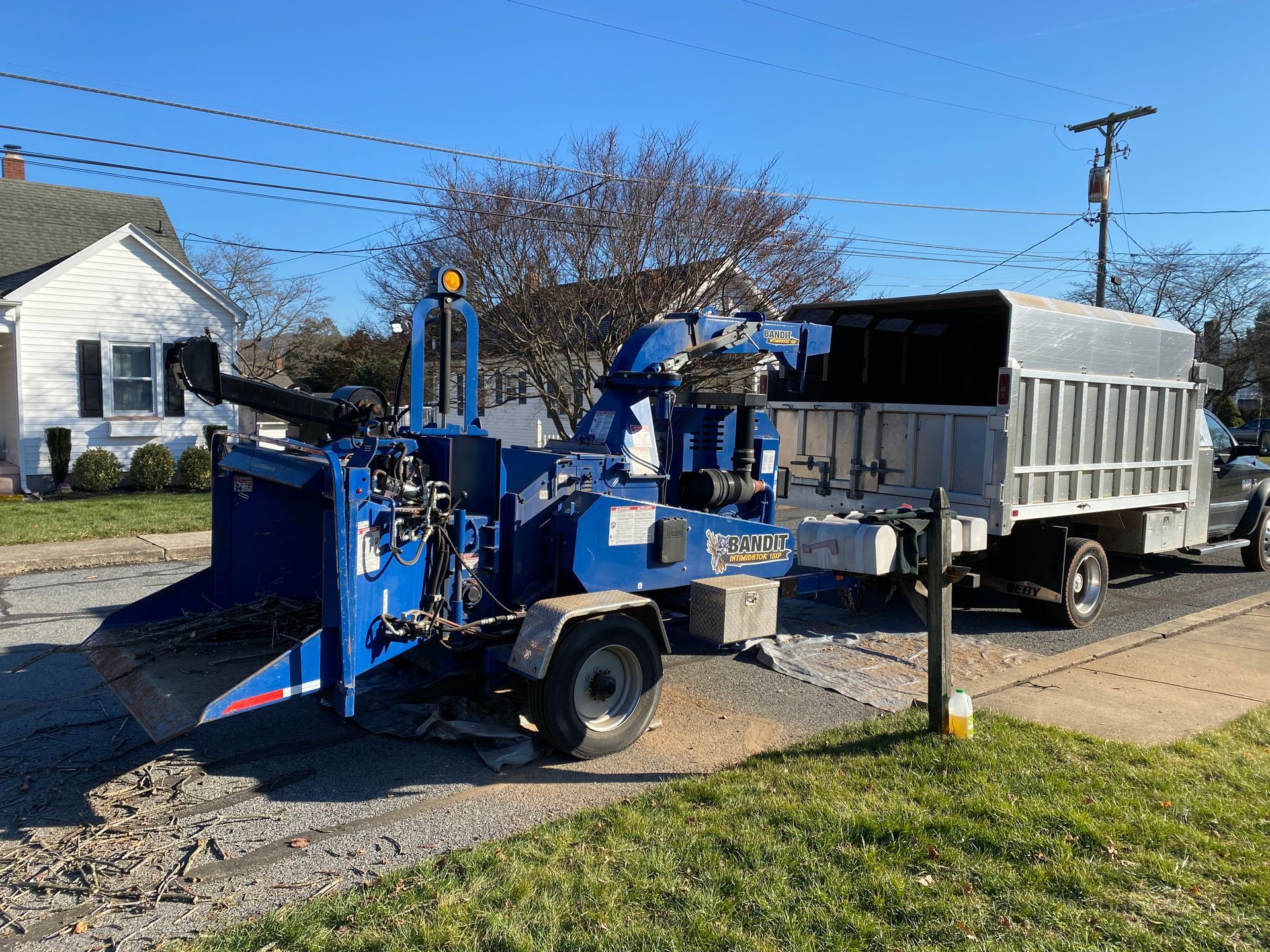 A blue tree chipper is parked on the side of the road next to a truck.