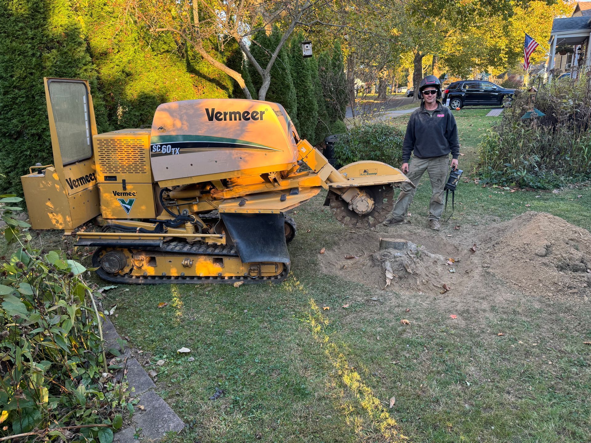 A man is standing next to a stump grinder in a yard.