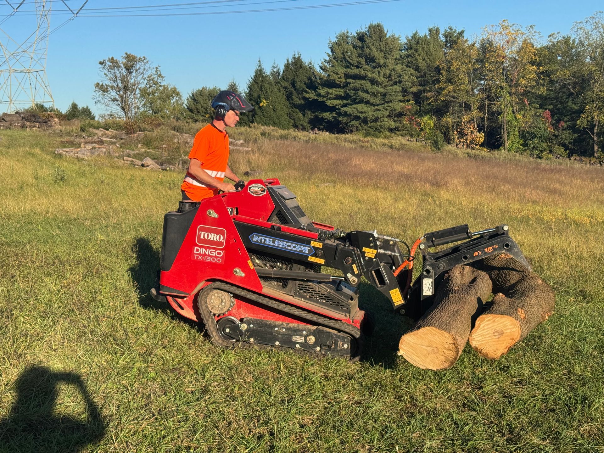 A man is riding a tractor in a field with logs.